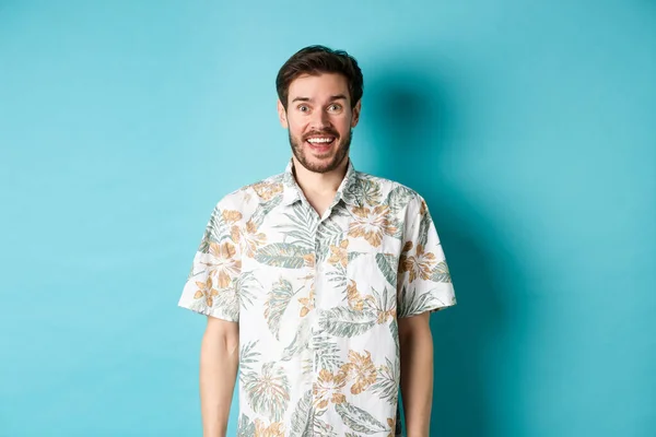 夏休みだ。ハワイのシャツのハンサムな幸せな男が面白がって、カメラで笑って、青い背景に立っている — ストック写真