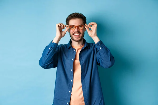 Homem caucasiano feliz tentando novos óculos e sorrindo, de pé sobre fundo azul — Fotografia de Stock