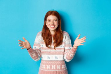 Büyük bir nesne tutan mutlu kızıl saçlı bir kız resmi. Şaşırmış görünüyor ve gülümsüyor, Noel hediyesi alıyor, mavi arka planda duruyor.