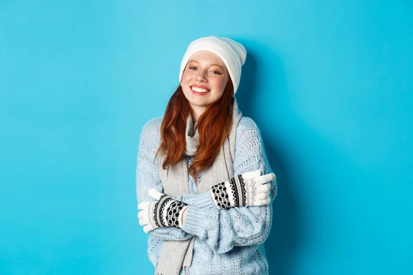 冬季和假日的概念。穿着便帽、手套和毛衣、头戴红头发、站在蓝色背景上、在外面暖烘烘的女孩 — 图库照片