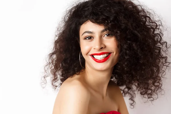 Close-up van vrolijke glimlachende vrouw met rode lippenstift en krullend kapsel, op zoek gelukkig, staande over witte achtergrond — Stockfoto