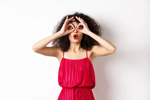 Impressed young woman seeing something awesome, look through hand binoculars and say wow, standing amazed at white background — Stock Photo, Image