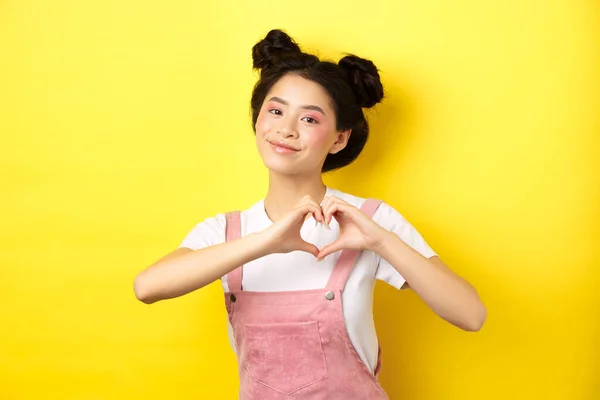 Dia dos Namorados. Bonito menina asiática enviando seu amor, mostrando gesto do coração e sorrindo para a câmera romântica, de pé no fundo amarelo — Fotografia de Stock