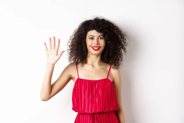 Cheerful young woman with makeup and red dress, showing five fingers and smiling, standing over white background — 图库照片