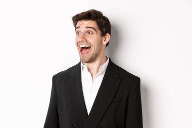 Takım elbiseli yakışıklı erkek girişimcinin yakın çekimi, sola bakıyor ve şaşkınlıkla gülümsüyor, beyaz arka plana karşı duruyor.