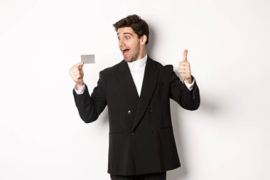Heyecanlı yakışıklı iş adamının görüntüsü, kredi kartı ve parmak kaldırma, beyaz arka plana karşı durmak