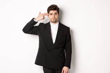 Sıkıntılı ve sorunlu takım elbiseli iş adamının portresi. Kafasına silah dayayıp rahatsız görünüyor, kendini vuruyor, beyaz arka plana karşı duruyor.