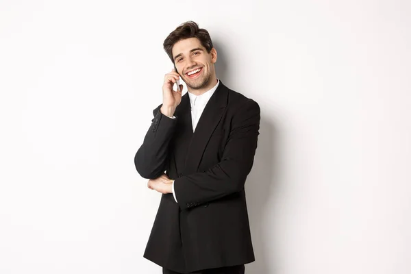 Bild av snygg, framgångsrik affärsman talar i telefon, leende nöjd, står i kostym mot vit bakgrund — Stockfoto