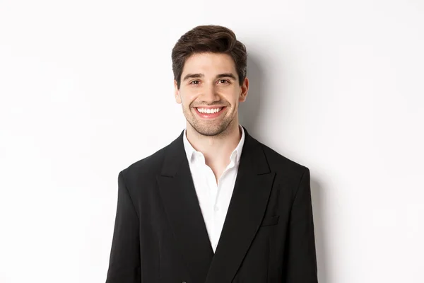 Närbild av stilig ung affärsman i trendig kostym leende, står mot vit bakgrund — Stockfoto