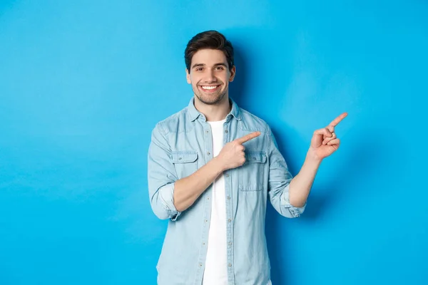 Retrato del atractivo hombre adulto sonriendo, señalando con los dedos el logotipo o la pancarta, mostrando publicidad sobre fondo azul — Foto de Stock
