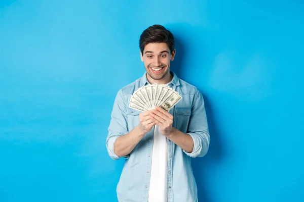 Emocionado hombre exitoso contando dinero, mirando satisfecho en efectivo y sonriendo, de pie sobre fondo azul — Foto de Stock