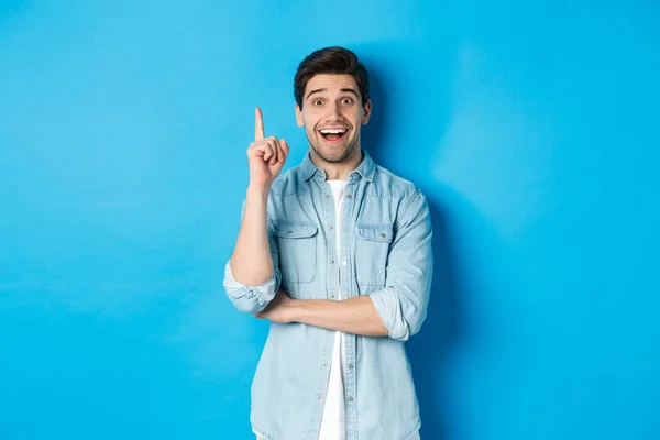 Imagen de hombre adulto guapo teniendo una idea, levantando el dedo y sonriendo excitado, solución encontrada, de pie sobre fondo azul — Foto de Stock