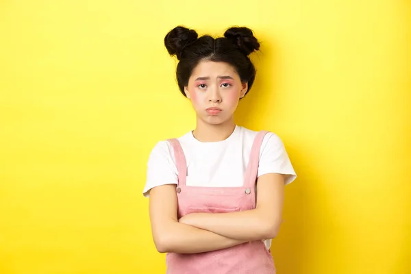 Smutné asijské dospívající dívka trucuje, křížové paže na hrudi, trucuje a mračí, stěžuje si na nespravedlivé věci, stojí na žlutém pozadí — Stock fotografie