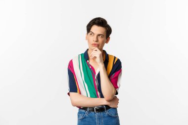 Yakışıklı, sol üst köşeye bakan, düşünen ya da seçim yapan, beyaz arka planda duran eşcinsel bir adam resmi.