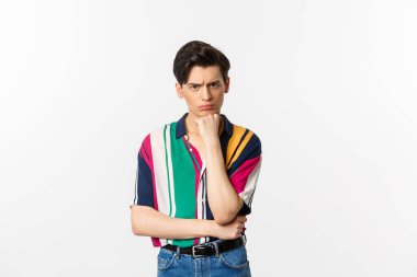 Hüzünlü gay adamın görüntüsü, kameraya bakıyor, somurtuyor ve üzgün, el üstünde duruyor, beyaz arka planda duruyor.