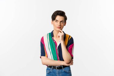 Yaratıcı genç adam düşünüyor ve gülümsüyor, sol üst köşeye bakıyor düşünceli, beyaz arka planda duruyor.