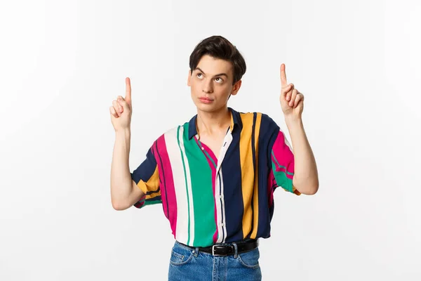 Привабливий гей-чоловік виглядає вдумливо, вказуючи пальці на логотип, стоячи над білим тлом — стокове фото