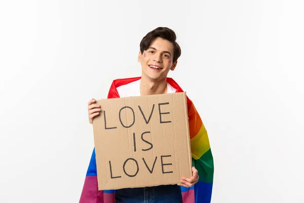 Gay sonriente activista hombre sosteniendo signo amor es amor para lgbt orgullo desfile, vistiendo arco iris bandera, de pie sobre blanco fondo —  Fotos de Stock