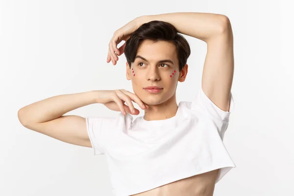 Close-up of beautiful androgynous man in crop top posing for camera, standing against white background — Stock Photo, Image