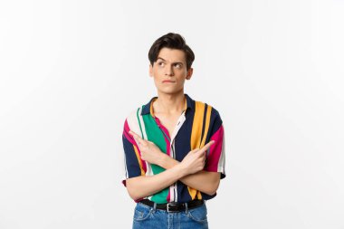 Kararsız yakışıklı bir adamın portresi seçim yapıyor, parmaklarını yana doğru gösteriyor ve düşünüyor, beyaz arka planda duruyor.