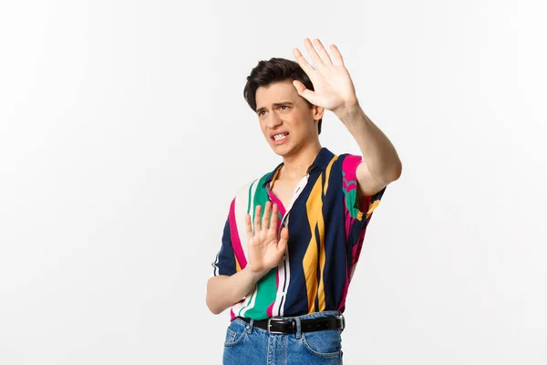 Timid and displeased androgynous man asking to stop, raising hands defensive and grimacing, standing over white background — Stock Photo, Image