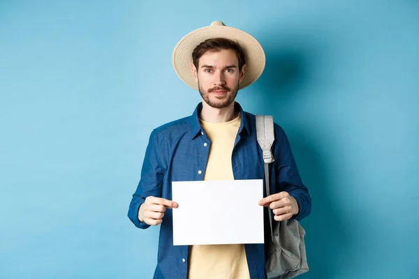 Immagine di ragazzo sorridente in paglia cappello zaino in spalla, autostop con pezzo di carta, viaggiare all'estero in vacanza estiva, sfondo blu — Foto Stock