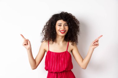 Kıvırcık saçlı, kırmızı dudaklı, gülümseyen beyaz dişli, iki tarafı gösteren, reklamları bir kenara bırakıp beyaz arka planda duran mutlu bir kadın.