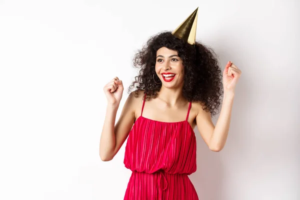 Felice compleanno ragazza che celebra, indossa cappello partito e vestito rosso, ballare e divertirsi, in piedi su sfondo bianco — Foto Stock