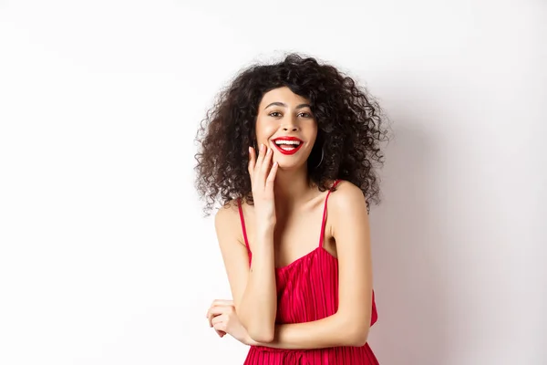 Ελκυστική γυναίκα με φόρεμα πάρτι, γελώντας και διασκεδάζοντας, χαμογελώντας χαρούμενη στην κάμερα, φορώντας μακιγιάζ κόκκινο κραγιόν, στέκεται σε λευκό φόντο — Φωτογραφία Αρχείου