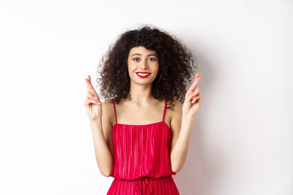 Chica de belleza esperanzada con el pelo rizado, dedos cruzados para la buena suerte y sonriendo, pidiendo deseo o orando, de pie sobre fondo blanco — Foto de Stock