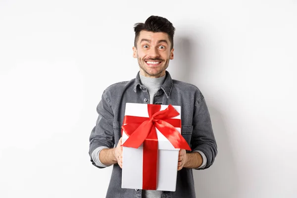 Веселый кавказский парень с сюрпризом подарок, получить подарок на праздник и улыбаясь благодарным, глядя благодарным в камеру, празднуя День Святого Валентина, белый фон — стоковое фото