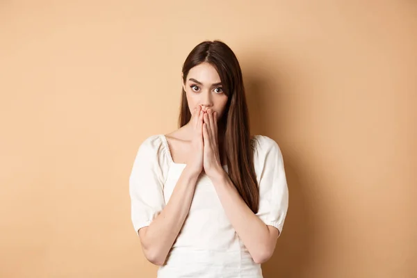 Omg chocante. Mulher sem fala cobrindo a boca com as mãos e olhando chocado para a câmera, fofocando, ouvir notícias deslumbrantes, fundo bege — Fotografia de Stock