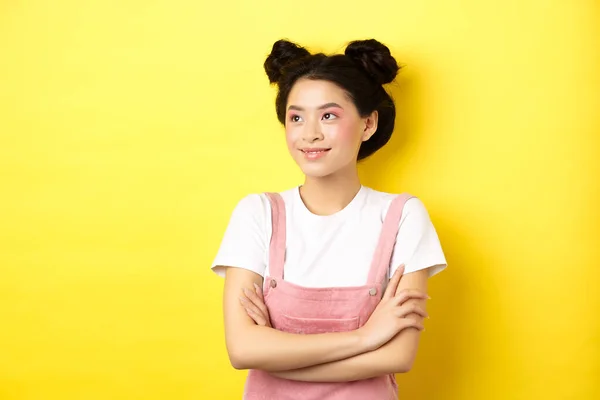 Sonriendo hermosa chica asiática con maquillaje glamour, mirando a un lado en el logotipo con la cara feliz, de pie en la ropa de verano sobre fondo amarillo — Foto de Stock