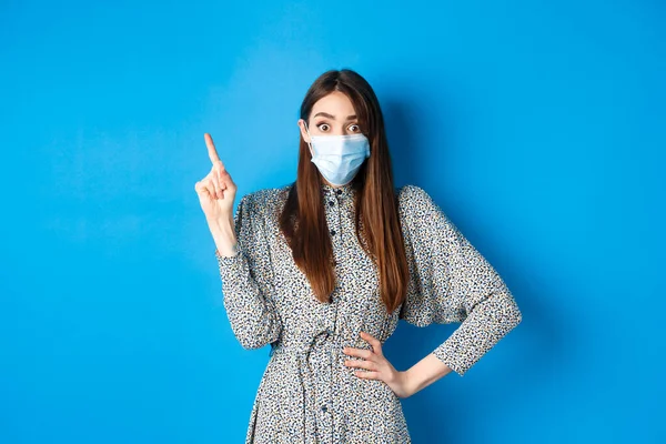 健康的人和covid-19大流行病概念。戴着医疗面具的兴奋女人指着左上角，站在蓝色的背景上 — 图库照片