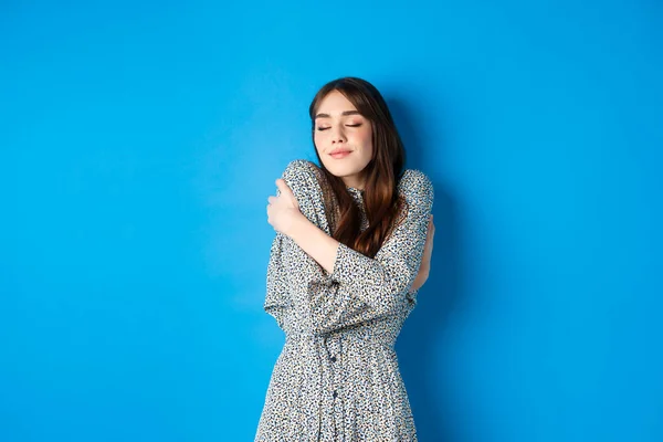 Romântico jovem mulher natural no vestido fechar os olhos, sorrindo e abraçando-se com amor e ternura, de pé sobre fundo azul — Fotografia de Stock