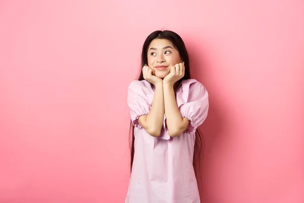 Ονειρεμένη ρομαντική κοπέλα κοιτάζοντας πέρα στο λογότυπο και χαμογελώντας, σκέφτεται κάτι όμορφο, στέκεται σε ροζ φόντο — Φωτογραφία Αρχείου