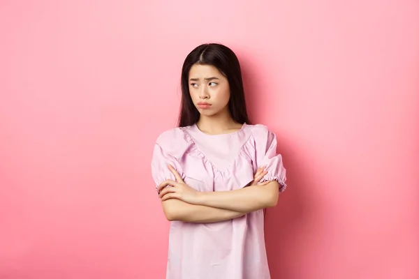 Triste y sombría mujer asiática mirar hacia otro lado en el logotipo, enfurruñado de la situación injusta, brazos cruzados en el pecho decepcionado, de pie sobre fondo rosa —  Fotos de Stock
