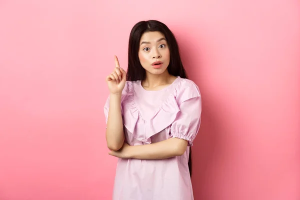 Podekscytowana azjatycka kobieta rzuca pomysł, wskazując palcem w znak Eureka, mają plan lub rozwiązanie, stojąc na różowym tle — Zdjęcie stockowe