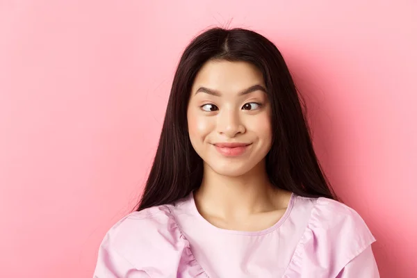 Primer plano retrato de divertido asiático mujer entrecerrando los ojos y haciendo tonto caras, de pie sobre rosa fondo —  Fotos de Stock
