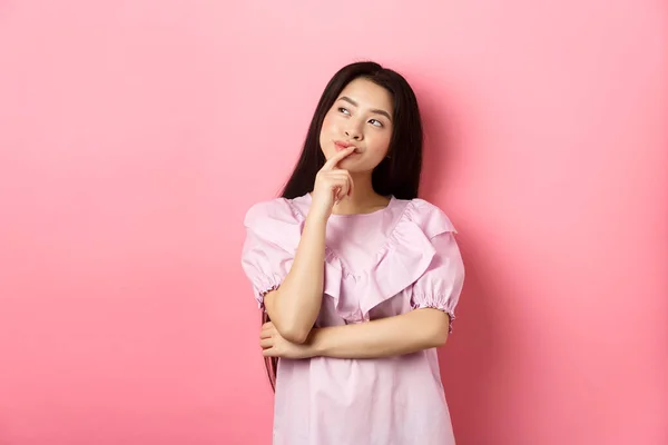 Pensivo sorrindo menina asiática fazendo escolha, olhando para o logotipo canto superior esquerdo e pensando, tendo uma ideia, de pé astúcia sobre fundo rosa — Fotografia de Stock