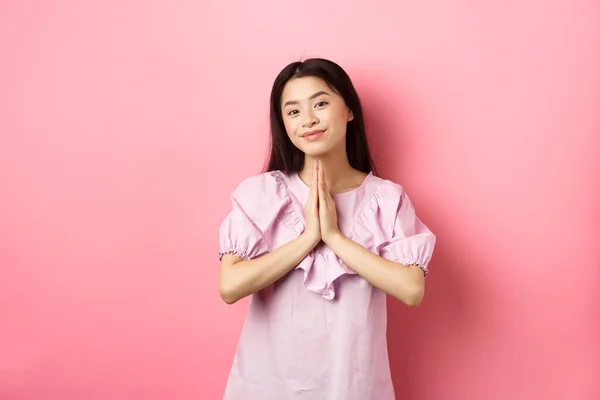Linda chica asiática decir gracias, sonriendo y mirando feliz, mostrando gesto namaste en gratitud, de pie en vestido sobre fondo rosa —  Fotos de Stock