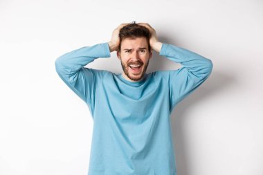 Hüsrana uğramış genç adam panik içinde çığlık atıyor, beyaz arka planda endişeli duruyor, panikliyor.