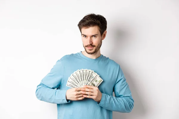 Hombre barbudo confiado sonriendo, mostrando dólares y mirando a la cámara. Chico guapo sosteniendo dinero sobre fondo blanco — Foto de Stock