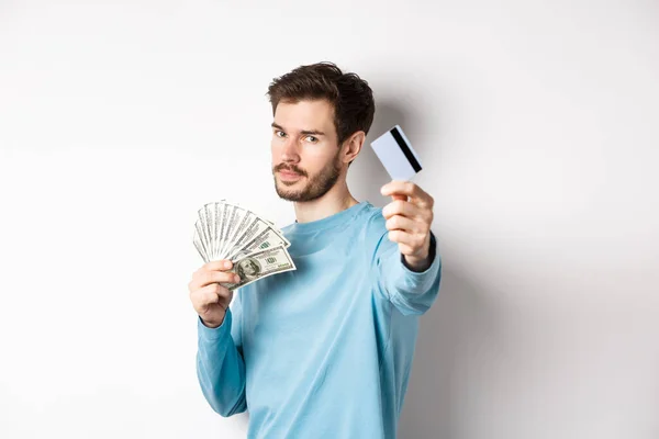Chico de aspecto serio estirar la mano con tarjeta de crédito de plástico, prefieren el pago sin contacto en lugar de dinero en efectivo, de pie sobre fondo blanco — Foto de Stock