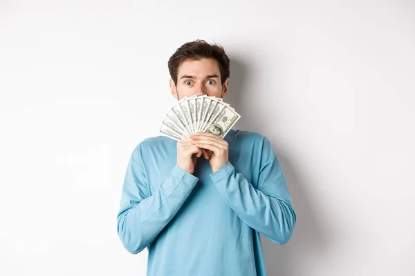 Sorprendido y sorprendido chico guapo mostrando dinero, mirando oferta promocional, ir de compras con dinero en efectivo, de pie sobre fondo blanco — Foto de Stock