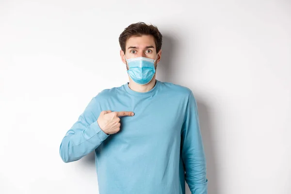 Coronavirus, έννοια της υγείας και της καραντίνας. Έκπληκτος τύπος με ιατρική μάσκα δείχνει τον εαυτό του, στέκεται πάνω από λευκό φόντο — Φωτογραφία Αρχείου