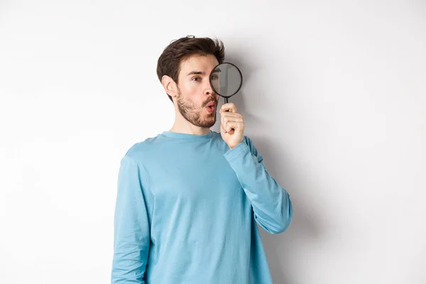 Curious guy looking through magnifying glass on right logo, saying wow, found cool thing, standing on white background — Stock Photo, Image