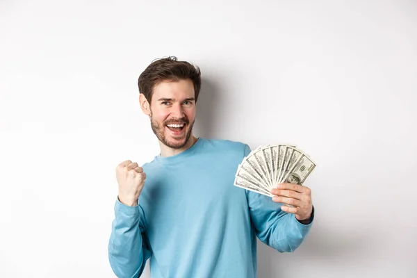 Hombre feliz bailando con dinero, mostrando dólares y diciendo sí con sonrisa satisfecha, haciendo gesto de bomba de puño, de pie sobre fondo blanco — Foto de Stock