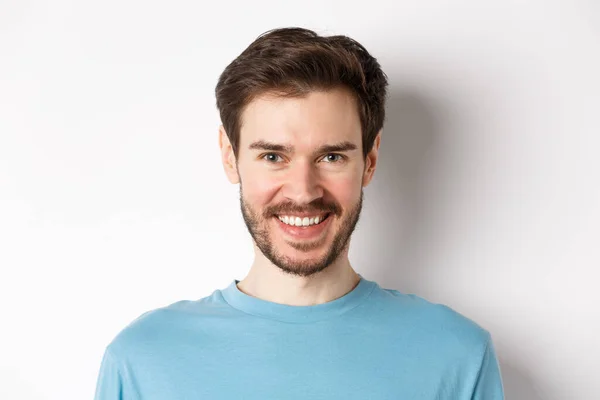 Close-up de belo homem caucasiano sorrindo com dentes brancos, olhando confiante para a câmera, de pé em camisa azul no fundo branco — Fotografia de Stock