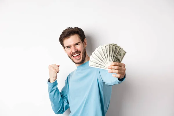 Hombre caucásico feliz estirar la mano con dinero en dólares, diciendo que sí y celebrando los ingresos, consiguió premio en efectivo, de pie sobre fondo blanco — Foto de Stock